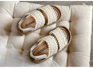 Detail view of girls bohemian crochet sandals with pom-poms on a soft cream cushion.