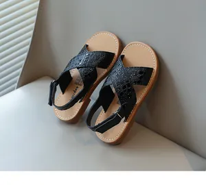 Primo piano di sandali neri per bambine con texture a coccodrillo e cuciture bianche