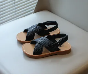 Dettaglio di sandali neri per bambini con motivo coccodrillo, cinturini incrociati e velcro.