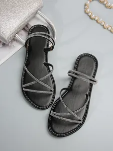 Elegantes sandalias planas negras con tiras cruzadas de pedrería y diseño minimalista.