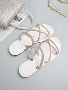 Primer plano de elegantes sandalias blancas planas con tiras cruzadas de pedrería.