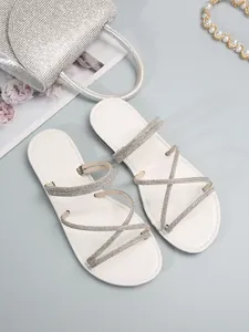 Sandalias planas blancas con tiras cruzadas de pedrería para un look elegante de verano.