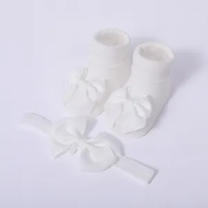 Primer plano detallado de un conjunto de calcetines y diadema blancos para bebé con lazos