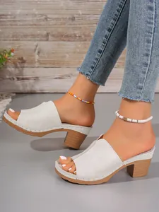 Nahaufnahme von weißen Peep-Toe-Mules mit klobigem Holzabsatz und bunten Fußkettchen.