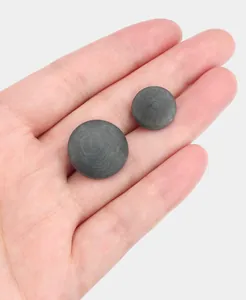 Dettaglio di bottoni naturali in noce di palma grigio scuro su una mano per scala e trama