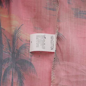 Detalle de la etiqueta de lavado 100% algodón en camisa hawaiana rosa con palmas