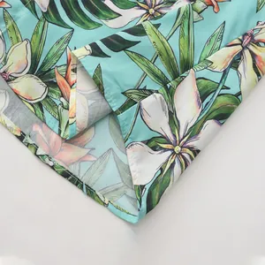 Detalle que muestra el patrón floral tropical en una camisa hawaiana turquesa para hombre.