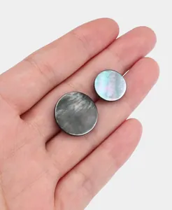 Close-up view of natural black lip shell buttons with iridescent luster on human palm.