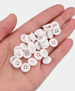 Close-up of white eco-friendly resin 4-hole shirt buttons held in a hand for scale