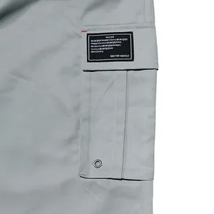 Détail de la poche cargo avec écusson décoratif noir sur un pantalon tissé gris