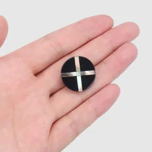 Detailansicht eines runden schwarzen Knopfes mit schillerndem Muschelkreuz-Inlay.