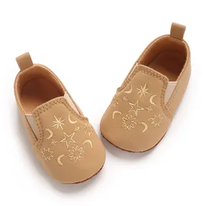 Detailansicht der bestickten Stern- und Mondmuster auf khakifarbenen Babyschuhen.