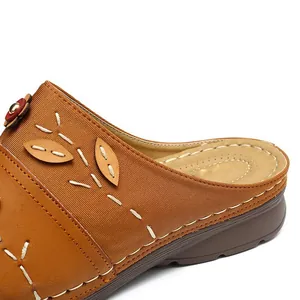 Close-up view of intricate decorative stitching and leaf appliqué on brown wedge sandals