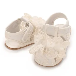 Detail von cremefarbenen Babysandalen mit zarten Spitzenausschnitten und Netzstoff