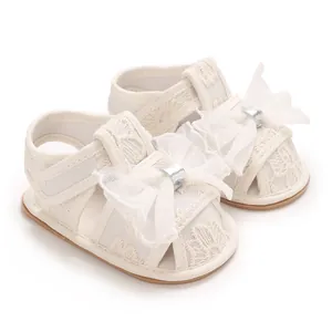 Detaillierte Makroansicht von beige Baby-Sandalen aus Spitze mit einer weißen Tüllschleife