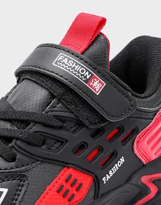 Gros plan d'une chaussure de course pour garçon noire et rouge à velcro.