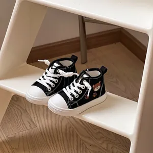 Primo piano di sneakers alte nere per bambini con ricamo a orsetto su uno sgabello