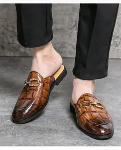 Close-up detail of men's brown crocodile embossed leather mules with gold buckle.