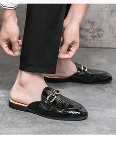Detailed close-up of men's black crocodile embossed patent leather mules with gold metal buckle