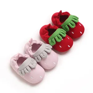 Vista detallada de lindos zapatos de piso para bebé con tema de fresa en rojo y rosa.
