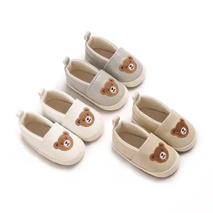 Colección de zapatos para primeros pasos de bebé con bordado de oso en gris, blanco y beige.