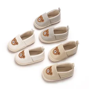 Vista detallada de zapatos para primeros pasos de bebé con oso bordado en blanco, gris y beige