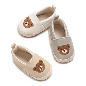 Vista detallada de tres zapatos de bebé con diseño de oso en crema, gris y beige.