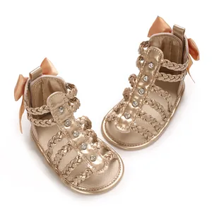 Detailansicht der goldenen Babysandalen mit Schleife, Flechtriemen und Strass