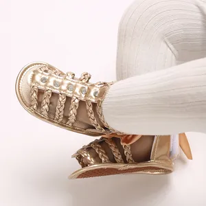 Detaillierte Nahaufnahme goldener Babysandalen mit geflochtenen Riemen und Strass