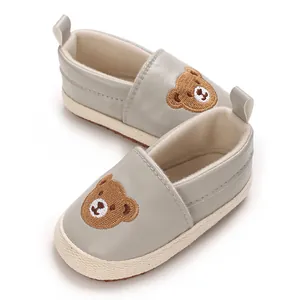 Detalle de zapatos de bebé grises con bordado de un lindo osito de dibujos animados.