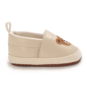 Vista detallada lateral de zapatos de bebé beige con bordado de oso lindo