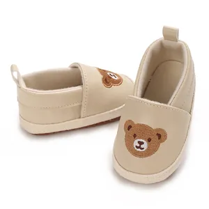 Primer plano de zapatos suaves beige para bebé con un lindo detalle bordado de oso marrón