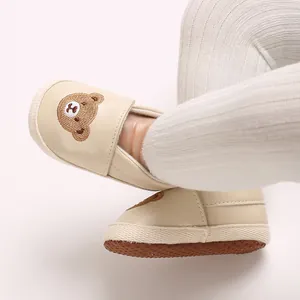 Vista detallada de mocasines crema para bebé con bordado de oso en zapatos para caminar.