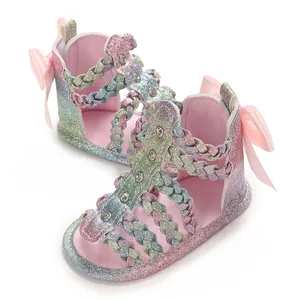 Detailansicht glitzernder Regenbogen-Babysandalen mit rosa Schleifen und geflochtenen Riemen.