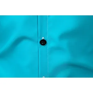 Detailed close-up of a black button and white stitching on a turquoise dress shirt