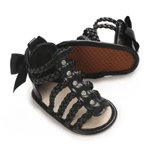 Detailansicht schwarzer Babysandalen mit geflochtenen Riemen, Strass und süßer Schleife.