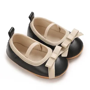 Close-up of black baby girl Mary Jane shoes with beige bow details and elastic strap.