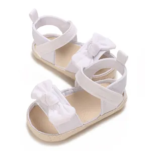 Primer plano de sandalias blancas para bebé con lazo decorativo y cierre de velcro.