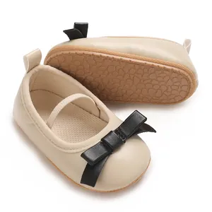 Close-up detail of beige baby girl princess shoes with black bow and anti-slip textured sole.