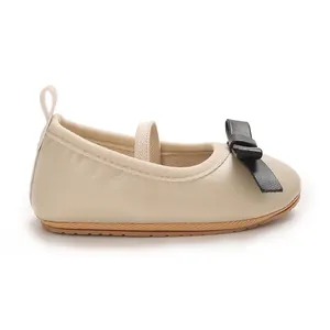 Close-up detail of beige baby girl princess flat shoes featuring a black bow and strap
