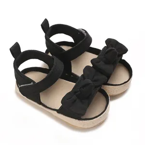 Detalle de sandalias negras para bebé niña con un lazo y suela de paja trenzada