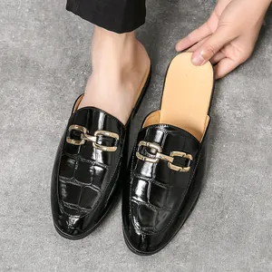 Men's black patent leather mule loafers with crocodile texture and gold chain buckle.