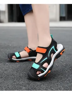 Close-up side view of boy's black closed-toe sandals with orange accents on asphalt road