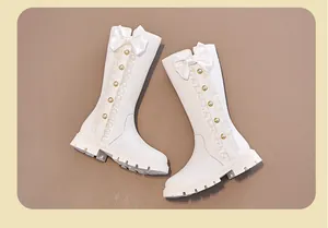 Macro view of white girls' high boots featuring elegant bow and pearl button accents