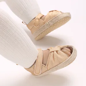 Closeup of champagne gold baby sandals with soft soles and knot design on white tights.