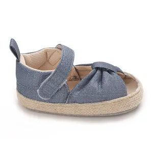 Close-up shot of a blue denim baby sandal featuring a knotted bow and woven espadrille sole.