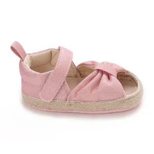 Detail view of a pink shimmer fabric baby sandal with soft sole and knotted design.