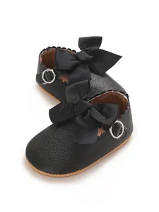 Detail view of black PU baby princess shoes with a large bow and scallop trim
