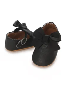 Close-up detail of black PU baby princess shoes with a large bow and scallop trim