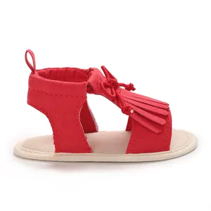 Side view detail of a red infant sandal with decorative fringe and bow